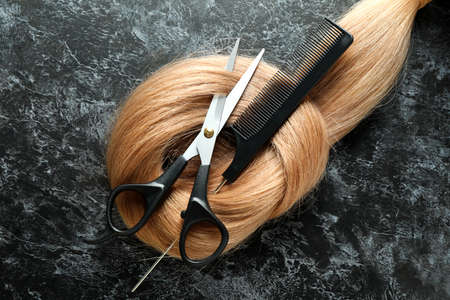Female hair with scissors and hairbrush on dark background