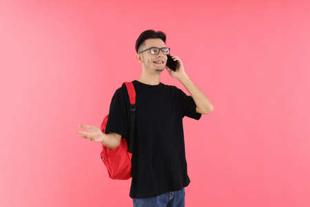 Attractive male student talking on the phone against pink backgroundの写真素材