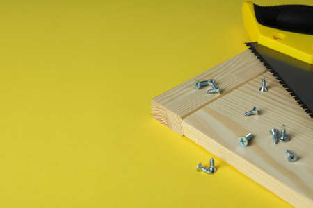 Saw, screws and wooden board on yellow background