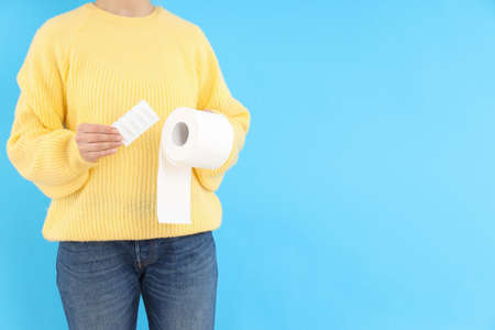 Woman holds toilet paper and suppositories on blue background. Hemorrhoids conceptの写真素材
