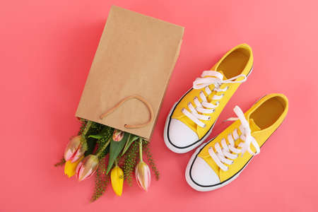 Sneakers and paper bag with flowers on pink background