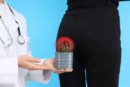 Doctor holds cactus on blue background with woman bottom. Hemorrhoids conceptの写真素材