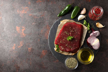 Concept of cooking with raw beef steak on dark textured background
