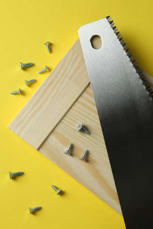 Saw, screws and wooden board on yellow backgroundの写真素材