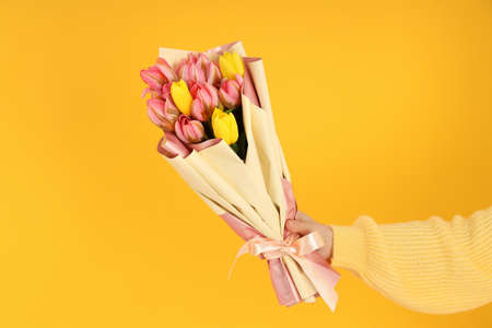 Woman's hand holding a bouquet on a yellow backgroundの写真素材