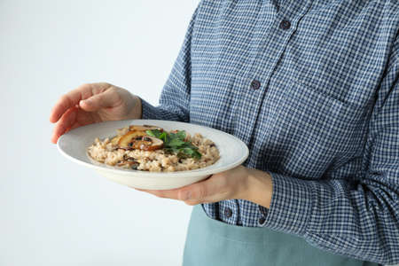 Woman in apron holds plate of risotto with mushroomsの写真素材