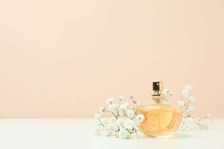 Perfume and flowers against beige background, space for text