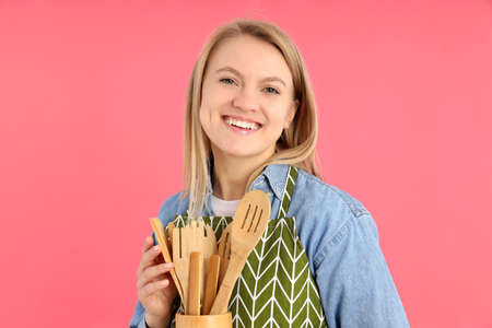 Housewife with wooden kitchen utensils on pink background