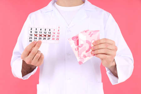 Doctor holds menstrual calendar and pads on pink backgroundの写真素材