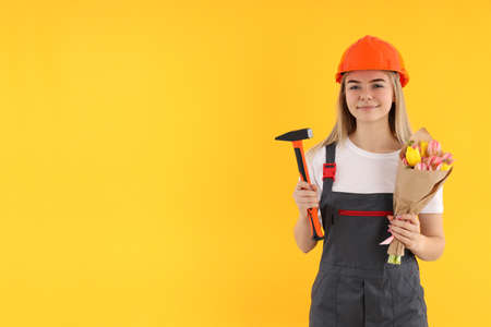 Builder woman with bouquet and hammer on yellow background