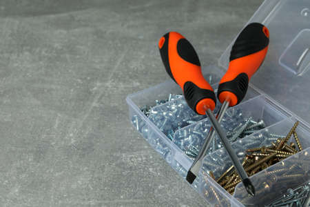 Box with screws and screwdrivers on gray textured background