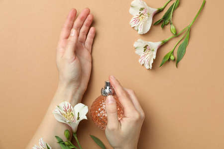Female hands hold bottle of perfume on beige background with flowersの写真素材