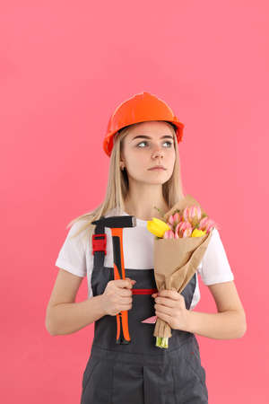 Builder woman with bouquet and hammer on pink backgroundの写真素材