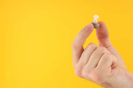 Male hand holding hearing aid on yellow background