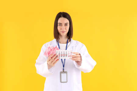 Trainee doctor with pads and period calendar on yellow backgroundの写真素材
