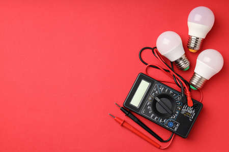 Multimeter and energy saving bulbs on red background