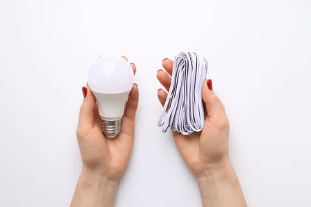 Female hands hold bulb and wire on white background