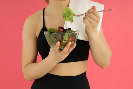 Concept of healthy lifestyle, woman eats salad on pink background