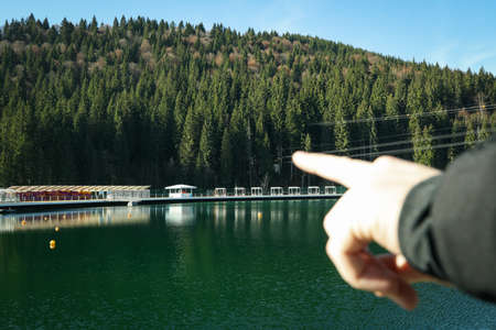 Hand point to something against lake and mountain forest