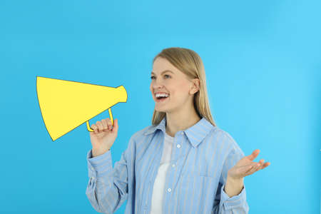 Young woman with megaphone on blue backgroundの写真素材