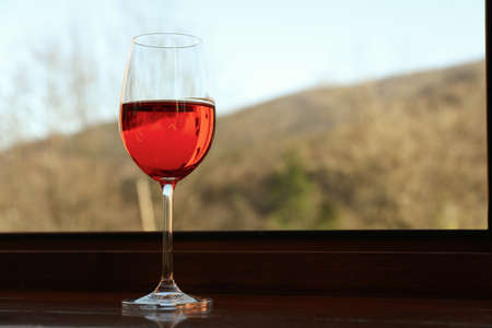 Glass of red wine stands on wooden windowsillの写真素材