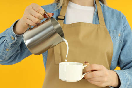Female barista pouring milk on yellow background