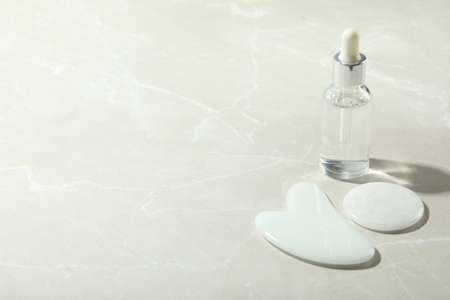 Face care concept with gua sha and cosmetic on light textured background