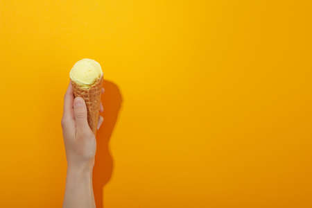Female hand with ice cream on orange background, space for text