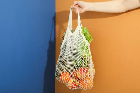 Female hand holds string bag with grocery on two tone backgroundの写真素材