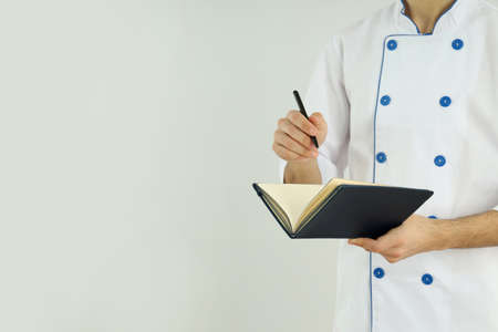 Young male chef with recipe book on light backgroundの写真素材