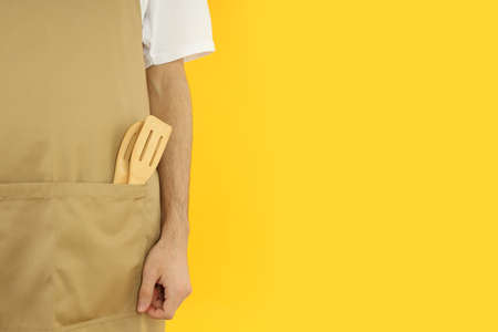 Young man in apron on yellow background, space for textの写真素材