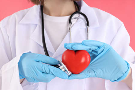 Female doctor holds stethoscope and heart on pink backgroundの写真素材