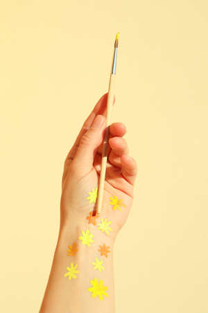 Female hand with painted flowers holds brush on beige backgroundの写真素材