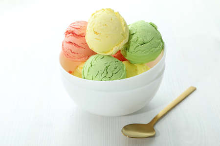 Bowl with ice cream scoops on white wooden tableの写真素材
