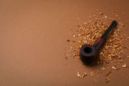 Smoking pipe with tobacco on brown background