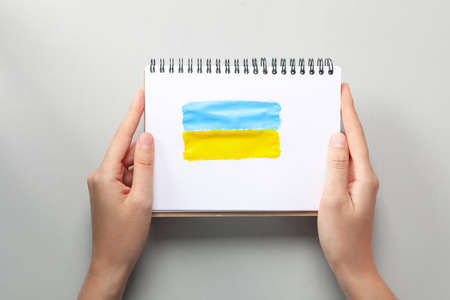 Female hands hold notebook with drawn Ukrainian flag on light gray backgroundの写真素材