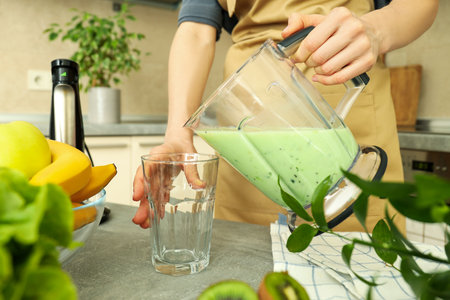 Woman pour smoothie from blender jug into glassの写真素材