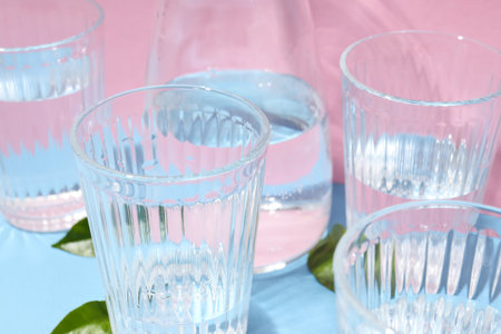 Jug and glasses of water, and leaves on two color background