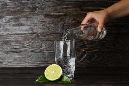 Female hand pour water in glass on wooden backgroundの写真素材
