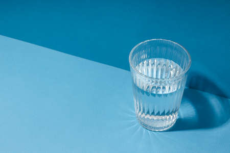 Glass of water on blue background, space for textの写真素材