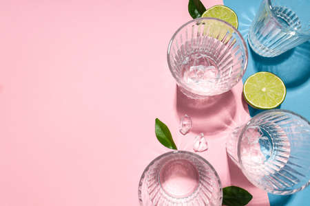 Glasses of water, lime, leaves and ice on two tone background