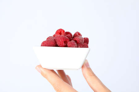 Female hand holds bowl with raspberries on white backgroundの写真素材
