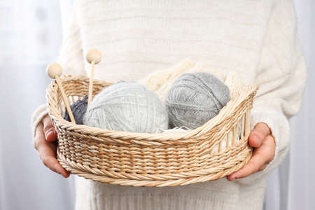 Woman in sweater holds wicker basket with knitting accessories