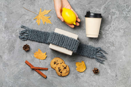 Female hand hold lemon on gray textured background with Autumn accessories