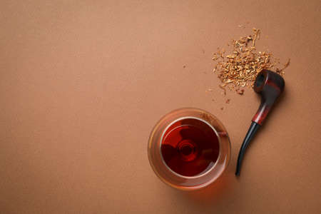 Smoking pipe, tobacco and glass of alcohol on brown backgroundの写真素材