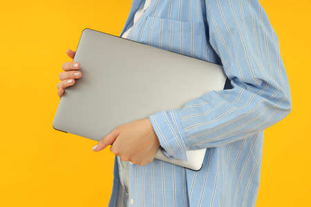 Young woman holding laptop on yellow backgroundの写真素材