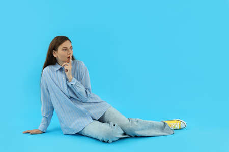 young woman with shhh gesture on blue backgroundの写真素材