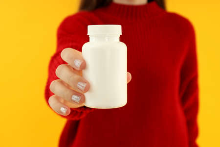 Young woman holding blank pill bottle on yellow backgroundの写真素材