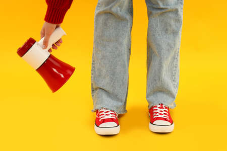 Woman in red sneakers holds megaphone on yellow background