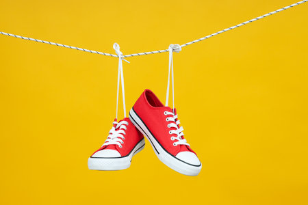 Pair of red sneakers hanging on twine on yellow backgroundの写真素材